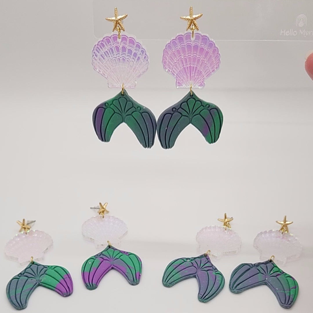 Pair of mermaid tail earrings with purple shells on a light gray background