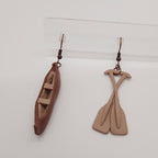 Pair of earrings shaped like a canoe and paddle on a white background